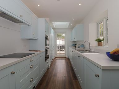 A galley kitchen with light blue cabinets dark wood floor and a door leading outside at Quay Cottage Sea View in Poole