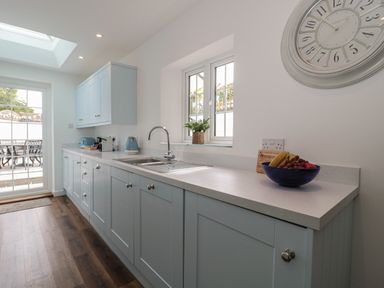 A kitchen with light blue cabinets a sink fruit bowl and wall clock at Quay Cottage - Sea View in Poole