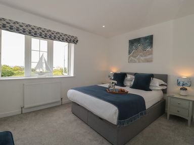 A bedroom with a double bed blue bedding bedside tables lamps and a window with a model sailboat at Quay Cottage - Sea View in Poole