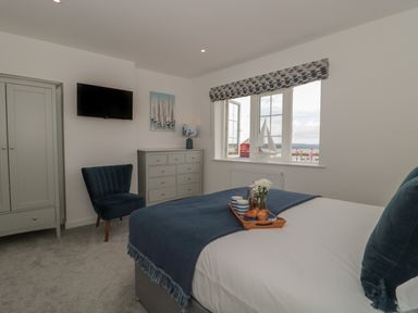 A bedroom with a blue chair dresser wall mounted tv and a bed with a tray near a window at Quay Cottage  Sea View in Poole