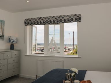 A bedroom with a dresser a lamp a bed and a window showing a marina at Quay Cottage Sea View in Poole