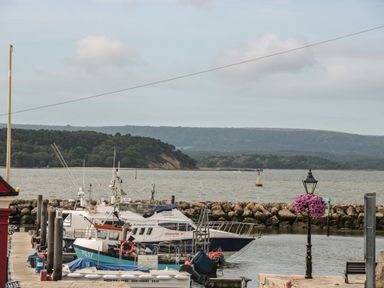 Boats docked at a pier with a stone breakwater and wooded hills in the background at Quay Cottage Sea View in Poole