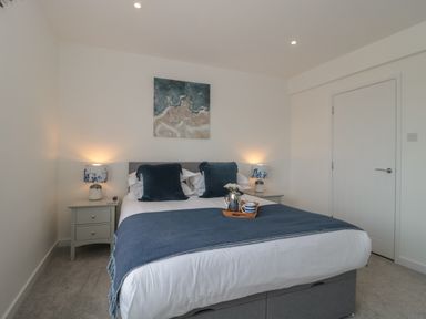 A bedroom with a double bed two bedside tables with lamps a door and a painting above the bed at Quay Cottage Sea View in Poole
