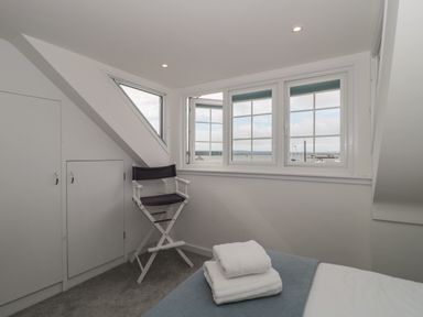 A bedroom corner with a window showing a sea view a director chair and folded towels on a bed at Quay Cottage - Sea View in Poole