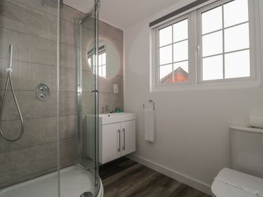 A bathroom with a glass shower enclosure a white vanity with mirror above window toilet and towel ring at Quay Cottage - Sea View in Poole
