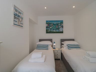 A bedroom with two single beds white bedding blue striped pillows a nightstand and two paintings on the walls at Quay Cottage - Sea View in Poole