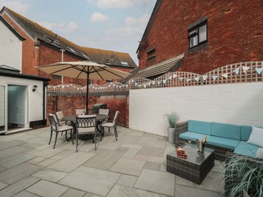 A patio with a round table and chairs under an umbrella and a seating area with a blue sofa and a coffee table at Quay Cottage Sea View in Poole