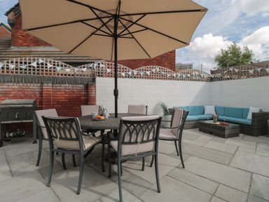 An outdoor patio with a round table and six chairs under an umbrella and a corner sofa with cushions at Quay Cottage - Sea View in Poole