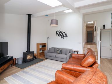 A living room with leather and fabric sofas a wood burning stove and a TV at 1 Orchard Cottages Dunstan near Craster