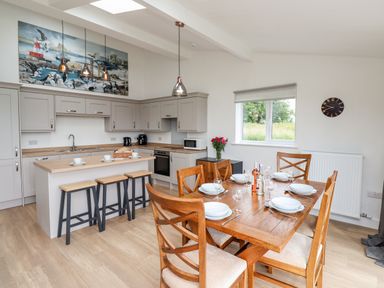 A kitchen with gray cabinets a wooden island with stools and a wooden dining table with chairs at 1 Orchard Cottages in Dunstan near Craster