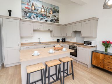 A kitchen with gray cabinets wooden countertops three stools at an island and flowers on a cabinet at 1 Orchard Cottages Dunstan near Craster