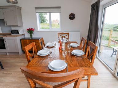 A dining area with a wooden table set for six and a kitchen corner visible at 1 Orchard Cottages Dunstan near Craster