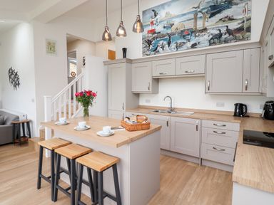 A kitchen with a wooden island counter with three stools and flowers in a vase at 1 Orchard Cottages in Dunstan near Craster
