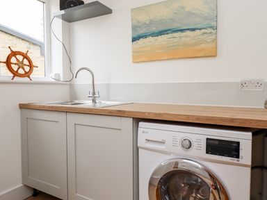 A kitchen area with a sink a washing machine a wooden countertop and a painting above the counter at 1 Orchard Cottages Dunstan near Craster