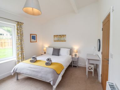 A bedroom with a bed with folded towels bedside tables lamps a desk and a window at 1 Orchard Cottages Dunstan near Craster