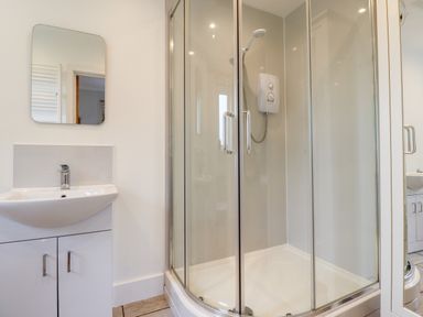 A bathroom with a shower enclosure and a sink with a mirror at 1 Orchard Cottages in Dunstan near Craster