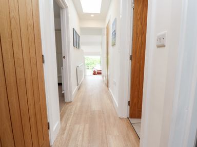 A hallway with wooden doors and light wood flooring leading to a room with a window and armchairs at 1 Orchard Cottages in Dunstan near Craster