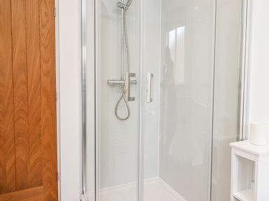 A shower enclosure with a wooden door and a small white shelf at 1 Orchard Cottages Dunstan near Craster