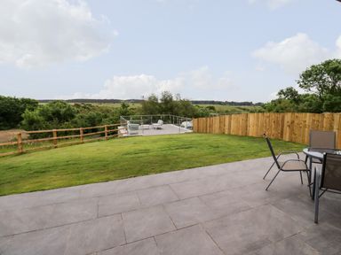 A patio with chairs and table overlooking a grassy yard with wooden and metal rail fences at 1 Orchard Cottages in Dunstan near Craster