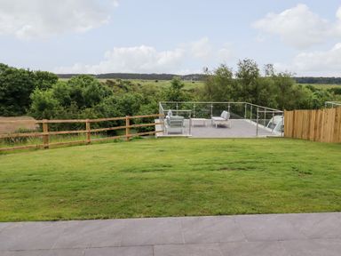 A grassy backyard with patio furniture on a deck and a wooden fence at 1 Orchard Cottages Dunstan near Craster