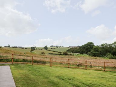A grassy backyard with a wooden fence overlooking fields and trees at 1 Orchard Cottages Dunstan near Craster