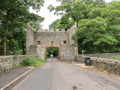 A stone archway over a narrow road surrounded by trees and stone walls at 1 Orchard Cottages Dunstan near Craster