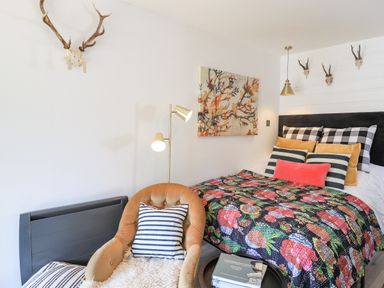 A bedroom with a bed decorated with patterned pillows and a floral quilt a chair with a striped pillow a floor lamp and skull decorations on walls at Creed Cabin in Stornoway