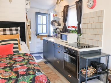 A small kitchen area with blue cabinets and a bed with colorful bedding and pillows at Creed Cabin in Stornoway