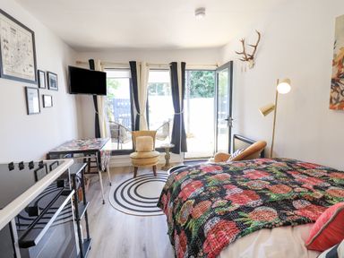 A bedroom with a bed covered with a floral quilt a small round chair and television mounted on a wall at Creed Cabin in Stornoway