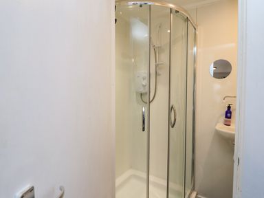 A bathroom with a glass shower enclosure and a small sink with a mirror and soap dispenser at Creed Cabin in Stornoway
