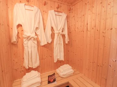 Two white robes hanging on wooden wall hooks with folded white towels on wooden benches and a sauna guide book at Creed Cabin in Stornoway