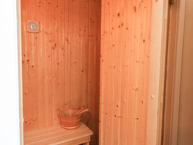 A wooden sauna interior with a bench a wooden bucket and ladle and a wall thermometer at Creed Cabin in Stornoway
