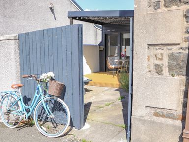 A blue bicycle leaning against a blue wooden gate with a patio area and chairs in the background at Creed Cabin in Stornoway