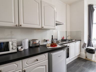 A kitchen with white cabinets microwave toaster kettle fridge and food on the counter at 4 Beach View Beaconsfield House in Bridlington