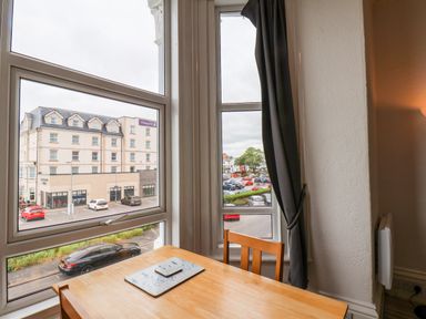 A room with a wooden table and chair next to windows showing a street and a building at 4 Beach View Beaconsfield House Bridlington