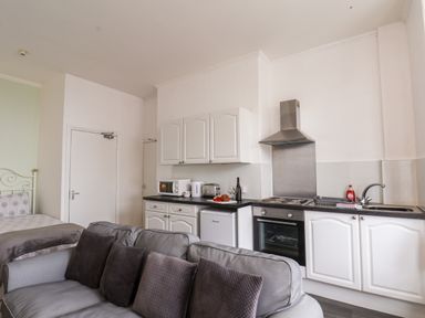 A kitchen area with white cabinets a sofa with pillows and a bed in the background at 4 Beach View Beaconsfield House Bridlington