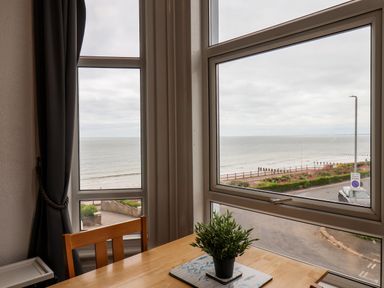 A wooden table with a small potted plant and a chair by windows overlooking the sea at 4 Beach View Beaconsfield House in Bridlington