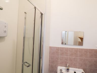 A bathroom with a shower cabin a mirror above a sink and a bottle of hand soap at 4 Beach View Beaconsfield House Bridlington