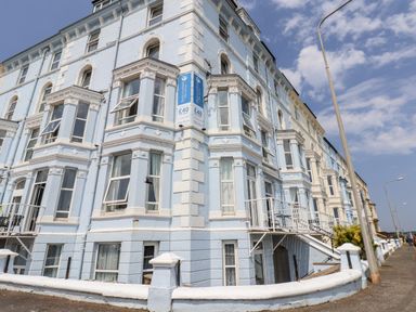 A blue multi-story building with white trim along a street with lamps at 4 Beach View @ Beaconsfield House Bridlington