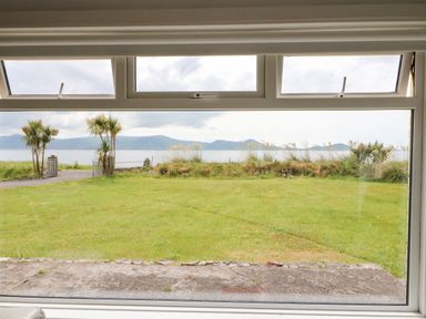 A large window view showing a lawn with palm trees and a body of water with mountains in the background at Meeligolleen in Coill Tra