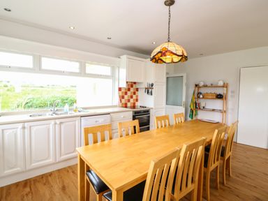 A kitchen with a wooden dining table and chairs a stove and cabinets with windows above at Meeligolleen in Coill Tra