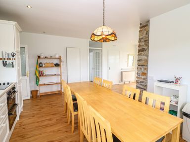 A dining area with a long wooden table and chairs kitchen appliances and shelves with kitchen items and books at Meeligolleen in Coill Tra
