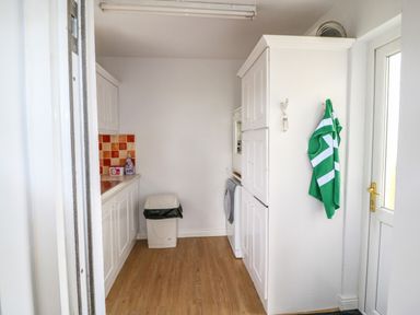 A laundry room with white cabinets a washing machine a trash bin and a green cloth hanging on the wall at Meeligolleen in Coill Tra