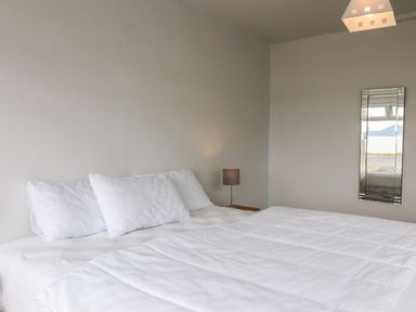 A bedroom with a bed with white bedding a bedside lamp and a wall mirror reflecting a window at Meeligolleen in Coill Tra