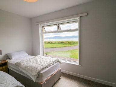 A bedroom with two single beds near a large window showing grass and mountains at Meeligolleen in Coill Tra