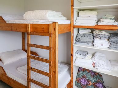A wooden bunk bed with white bedding next to a shelving unit with folded linens at Meeligolleen in Coill Tra