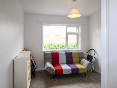 A small room with a multicolored sofa under a window and a white shelf on the left at Meeligolleen in Coill Tra