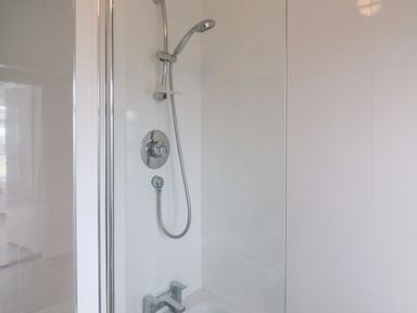 A shower area with a handheld showerhead and faucet in a tiled bathroom at Meeligolleen in Coill Tra