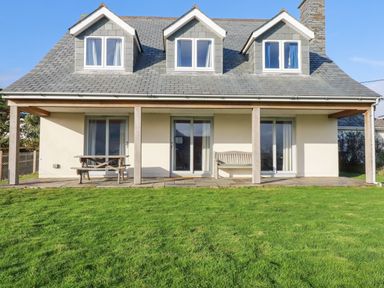 A house with three dormer windows a patio with a wooden bench and picnic table and a lawn in front at Freefolk in Polzeath