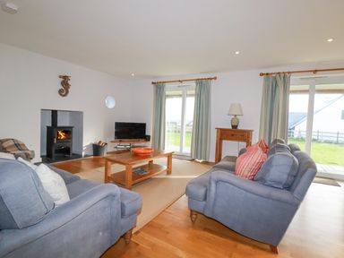 A living room with two blue sofas a wooden coffee table a TV a wood burning stove and large windows at Freefolk in Polzeath